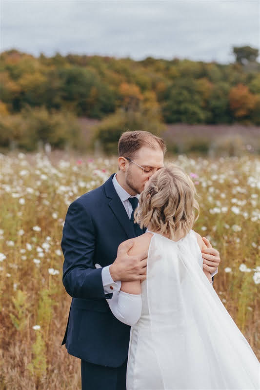 Couple kissing in a field of cosmos after their first look during their Cherry Basket Farm wedding. 