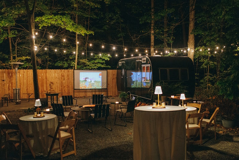 Evening outdoor setting including a bonfire pit, cocktail tables with ivory linens and LED table lamps during October wedding reception at Cherry Basket Farm. 