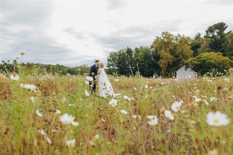 A field of cosmos with a bride and groom kissing after their first look during their Cherry Basket Farm wedding. 
